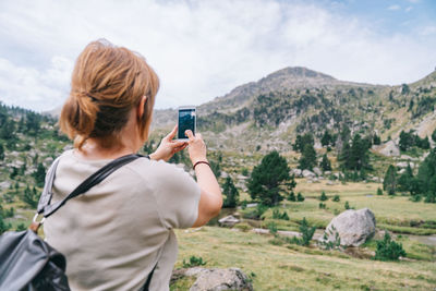 Rear view of woman photographing on mountain against sky