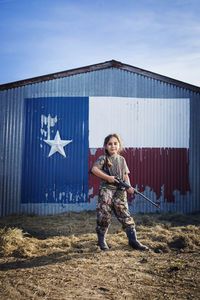 Portrait of girl with rifle standing on field against texas flag