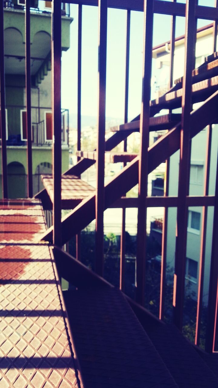 built structure, architecture, window, railing, sunlight, building exterior, glass - material, shadow, empty, indoors, day, chair, absence, transparent, sky, no people, city, metal, fence