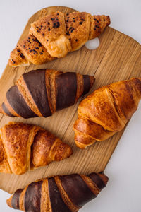 Flat lay of bunch of appetizing brown and chocolate croissants on a wooden board on white table	