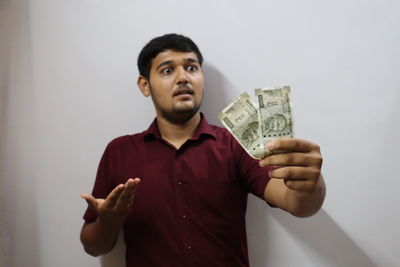 Young man holding camera standing against wall
