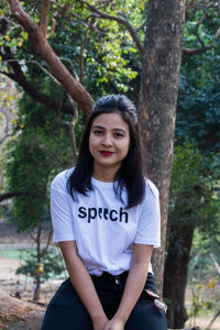 Portrait of young woman sitting on tree trunk in forest