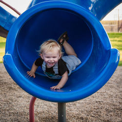 Full length of cheerful boy sliding in blue slide at playground