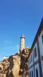 Low angle view of lighthouse by building against clear blue sky