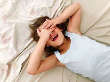 Girl covering eyes with hands while lying on bed