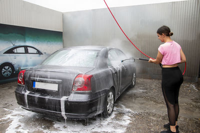 Cute teen girl cleans automobile with foam shampoo chemical detergents during carwash self service
