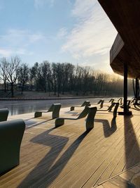 Empty chairs by bare trees against sky
