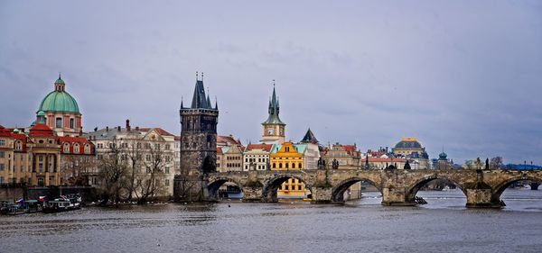 Arch bridge over river by buildings against sky