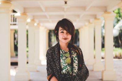 Portrait of smiling young woman standing against wall