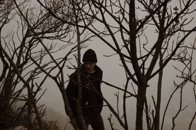 Man standing by bare tree during winter