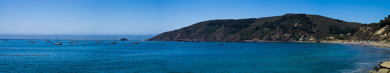 Scenic view of sea and mountains against clear blue sky