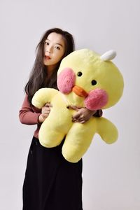 Portrait of young woman holding stuffed toy while standing against white background