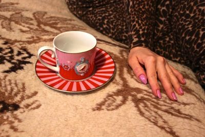 Midsection of woman sitting by empty cup and saucer on sofa