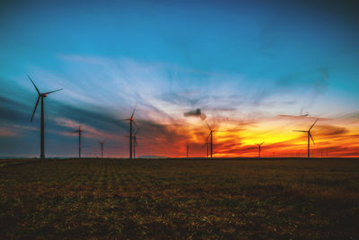 Windmills on field against sky during sunset
