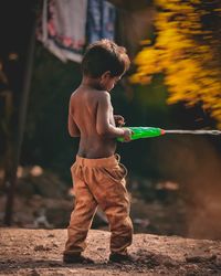 Full length of shirtless boy holding squirt gun while standing on land
