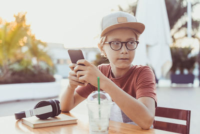 Boy using phone while sitting at outdoor cafe