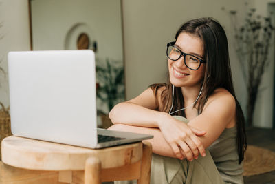 A young brunette woman in glasses is watching video using a laptop and headphones.