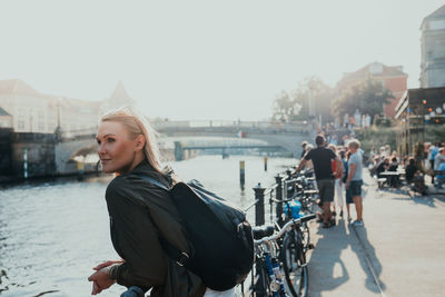 Young woman looking away while standing by railing in city against sky