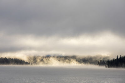 Thick mist over calm lake water and overcast sky during sunrise