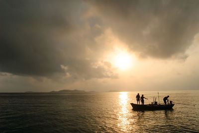 Silhouette people in sea against sky during sunset