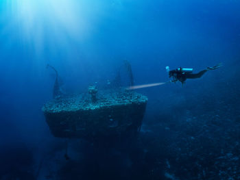 Person swimming in sea by shipwreck