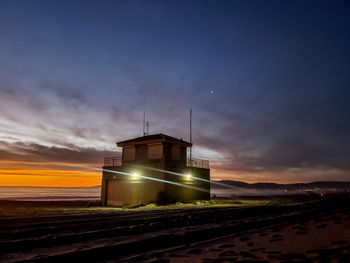 Building by sea against sky at sunset