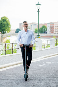 Young businessman in a suit riding an electric scooter while commuting to work in city