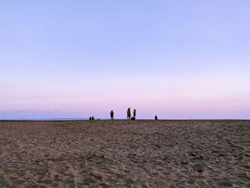 People at beach against sky during sunset