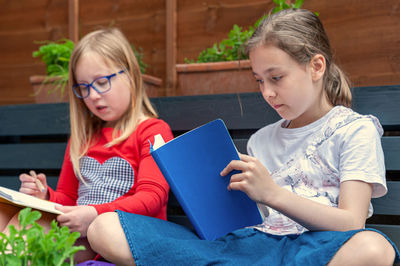 Two school age girls sitting together in garden and doing homework.