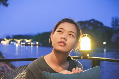 Portrait of young woman against illuminated railing at night