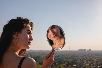 Rear view of young woman looking in mirror against clear sky