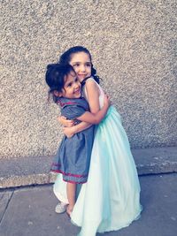 Cute sisters embracing while standing against wall