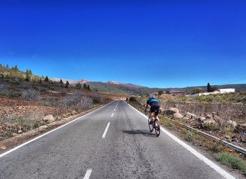 Man riding bicycle on road against clear blue sky