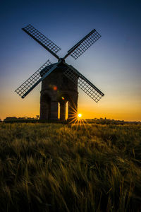 Traditional windmill on field against sky at sunset