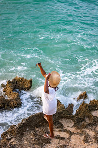 Rear view of young woman standing at beach photographing 