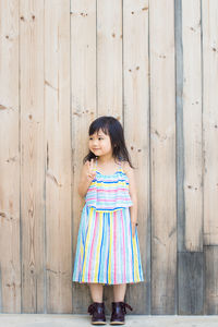 Full length of girl standing against wooden wall