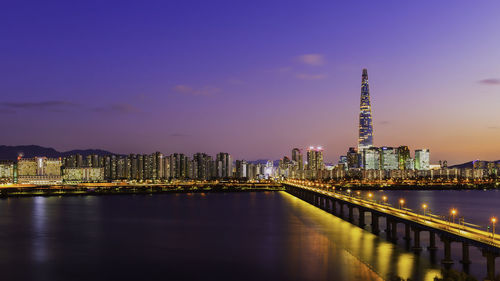 Illuminated buildings by river against sky at night