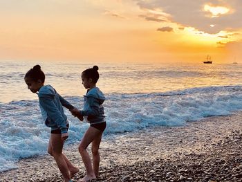 Girl holding hand of sister on shore at beach during sunset
