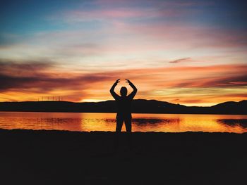 Silhouette woman posing at lakeshore against sky during sunset