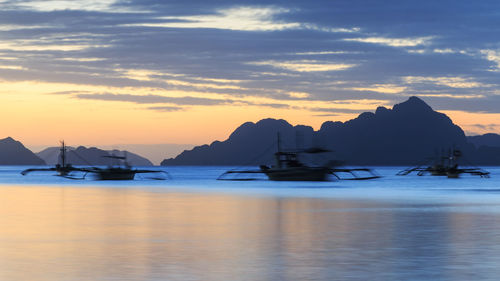 Boats in calm sea at sunset