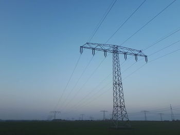 Low angle view of electricity pylon on field against clear sky