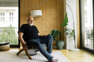 Depressed mature man sitting on chair in living room at home