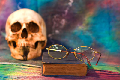 Close-up of book and eyeglasses against skull on table during halloween