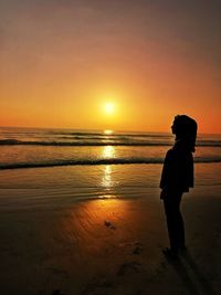 Silhouette man standing on beach against sky during sunset