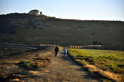 Rear view of people walking on field against sky