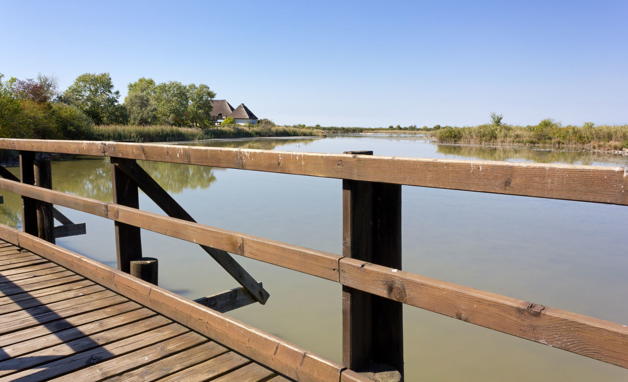 WOODEN BRIDGE OVER LAKE AGAINST CLEAR SKY
