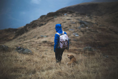 Rear view of person with dog on grassy mountain