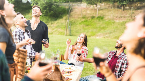 Friends laughing while having wine at park during picnic