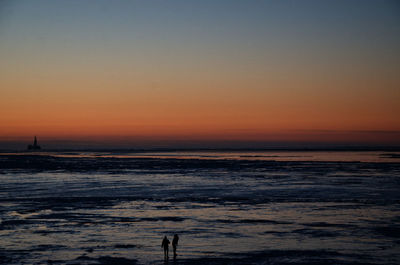 Silhouette people standing on frozen sea against sky during sunset