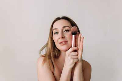 A beautiful natural woman makeup artist preens herself with makeup on a white isolated background